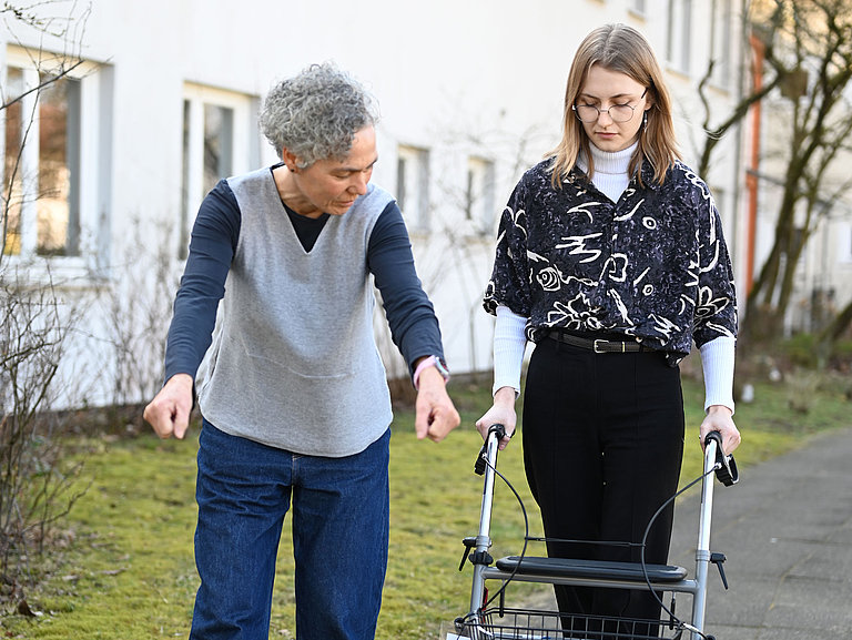 Eine Auszubildende übt mit einem Rollator eine Alltagssituation im Freien.